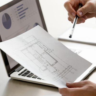 Male hand holding project plan, statistics on screen, close up Close up view of male hand holding project plan, financial statistics data on laptop screen at background, analyzing real estate market, mortgage loan with low rate, construction investment